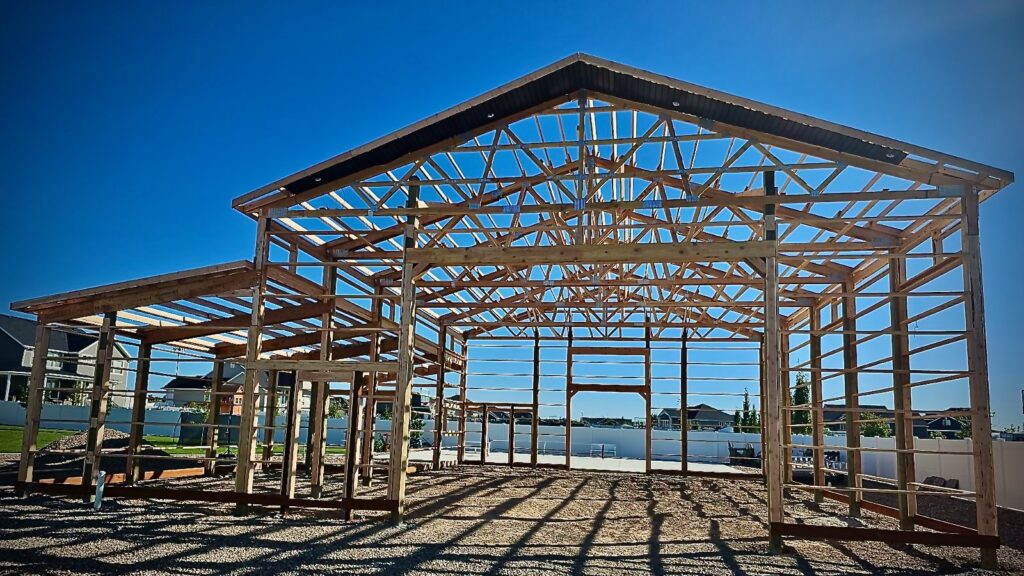 Framework of a pole barn structure in progress, showcasing the sturdy skeletal construction and architectural design.