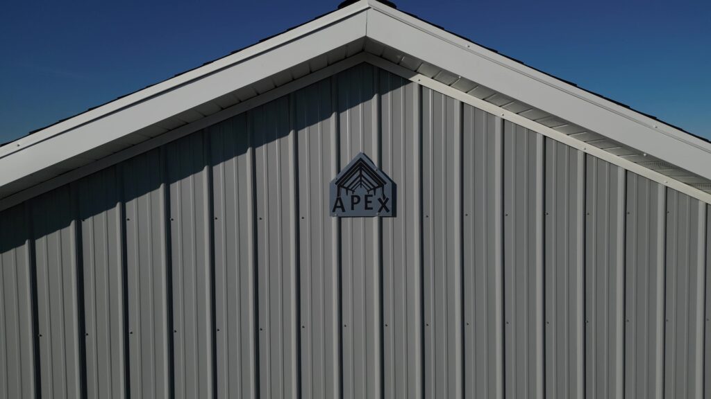 Apex Structures logo prominently displayed on the side of a modern pole barn, symbolizing quality construction and design.