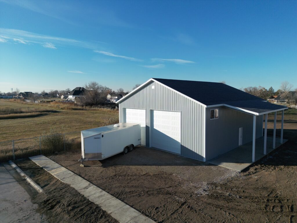 Spacious pole barn and lean-to with asphalt shingle roof and large garage doors, set against a backdrop of clear blue skies.